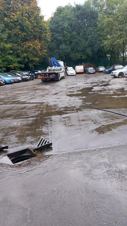 Commercial blocked drain being cleared with heavy machinery in a parking lot.
