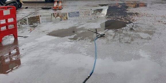 Drainage team working outside industrial warehouse on wet day with equipment.