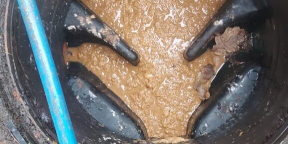Blocked drain in a commercial setting with water and debris inside a manhole.