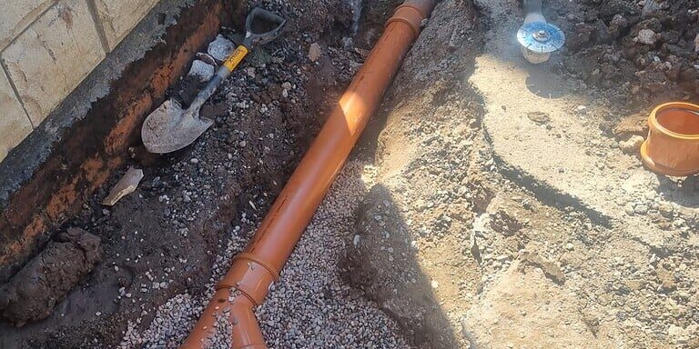 Underground drainage pipe installation with orange PVC pipes and fittings for effective property dra.